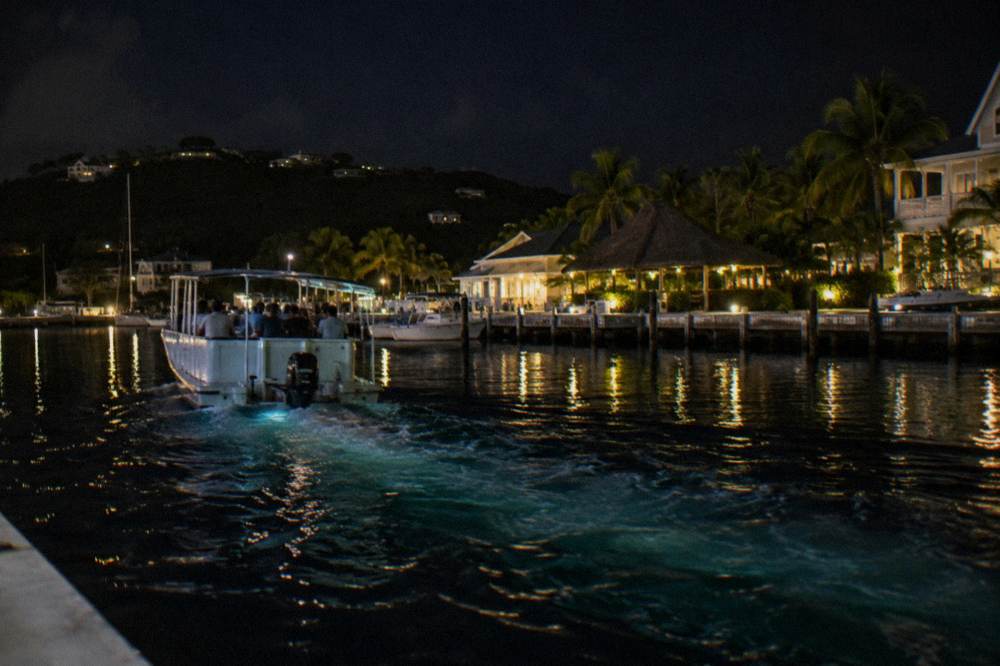 A tour boat on dark water at night with a faint blue-green glow trailing behind the hull